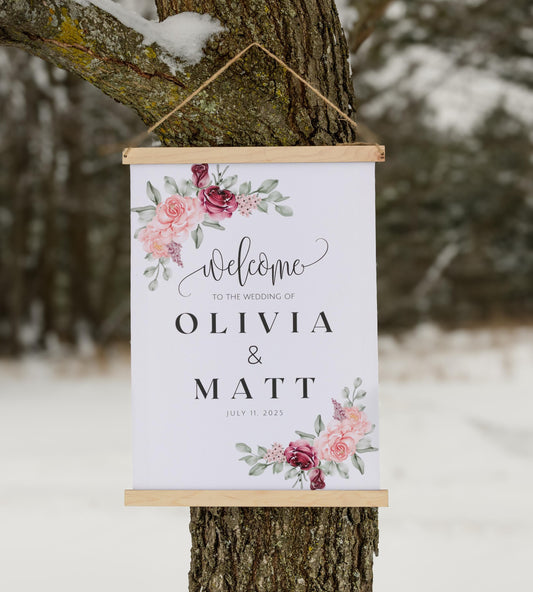 custom welcome to our wedding sign, ceremony entrance, reception entrance wedding decor, personalized with welcome message, couples names and date of venue, accented with floral designs in the corners, sign has wood top & bottom, it is made from canvas, it hangs freely with a rope on top.