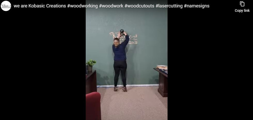 Load video: laser machine cutting wood signs, cutting out our kobasic creations logo, then mounting on wall using nail gun