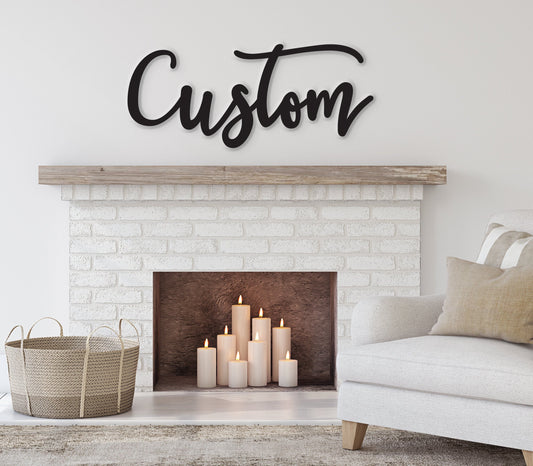 May include: A white brick fireplace with a wooden mantel above it. The fireplace has a black metal surround and a wood-burning fire inside. There are several lit candles in front of the fireplace. Above the mantel is a black metal sign that says 'Custom' in a cursive font. A white couch with a tan throw pillow is in the foreground.
