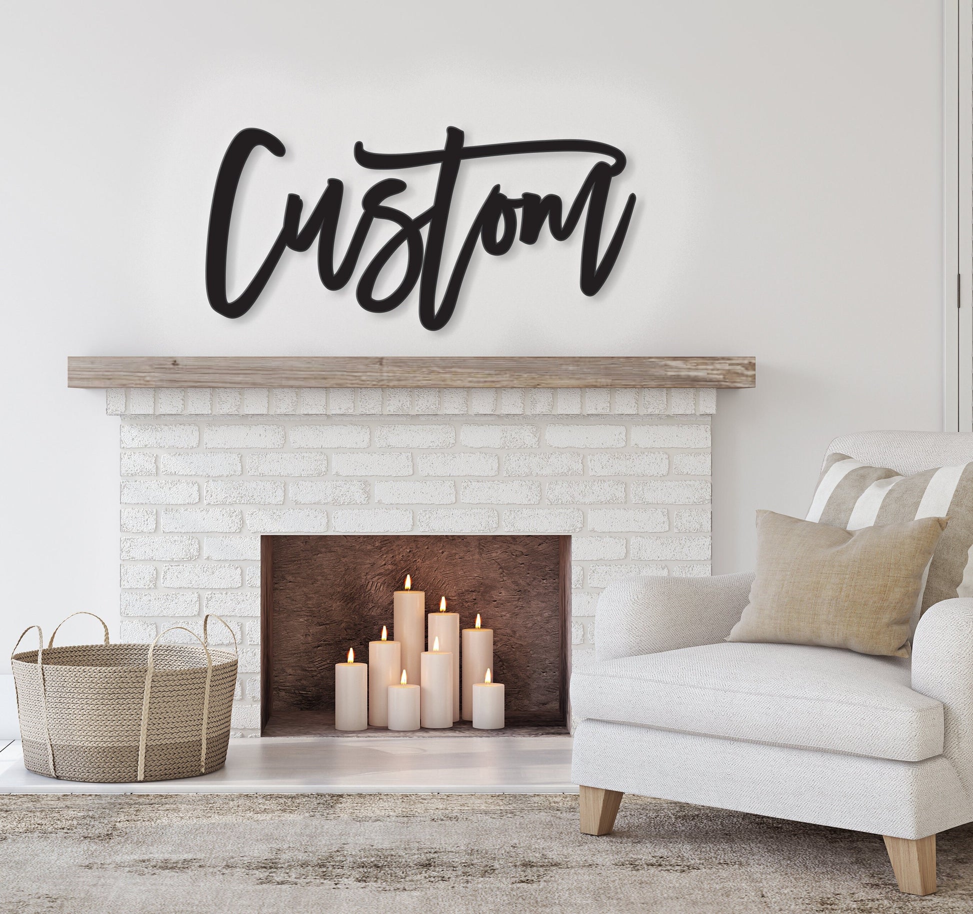 May include: A white brick fireplace with a black metal mantel above it. The word 'Custom' is written in black script on the mantel. The fireplace has a black hearth and a white brick surround. There are six white candles in the fireplace. A white armchair with a tan throw pillow is in the foreground.